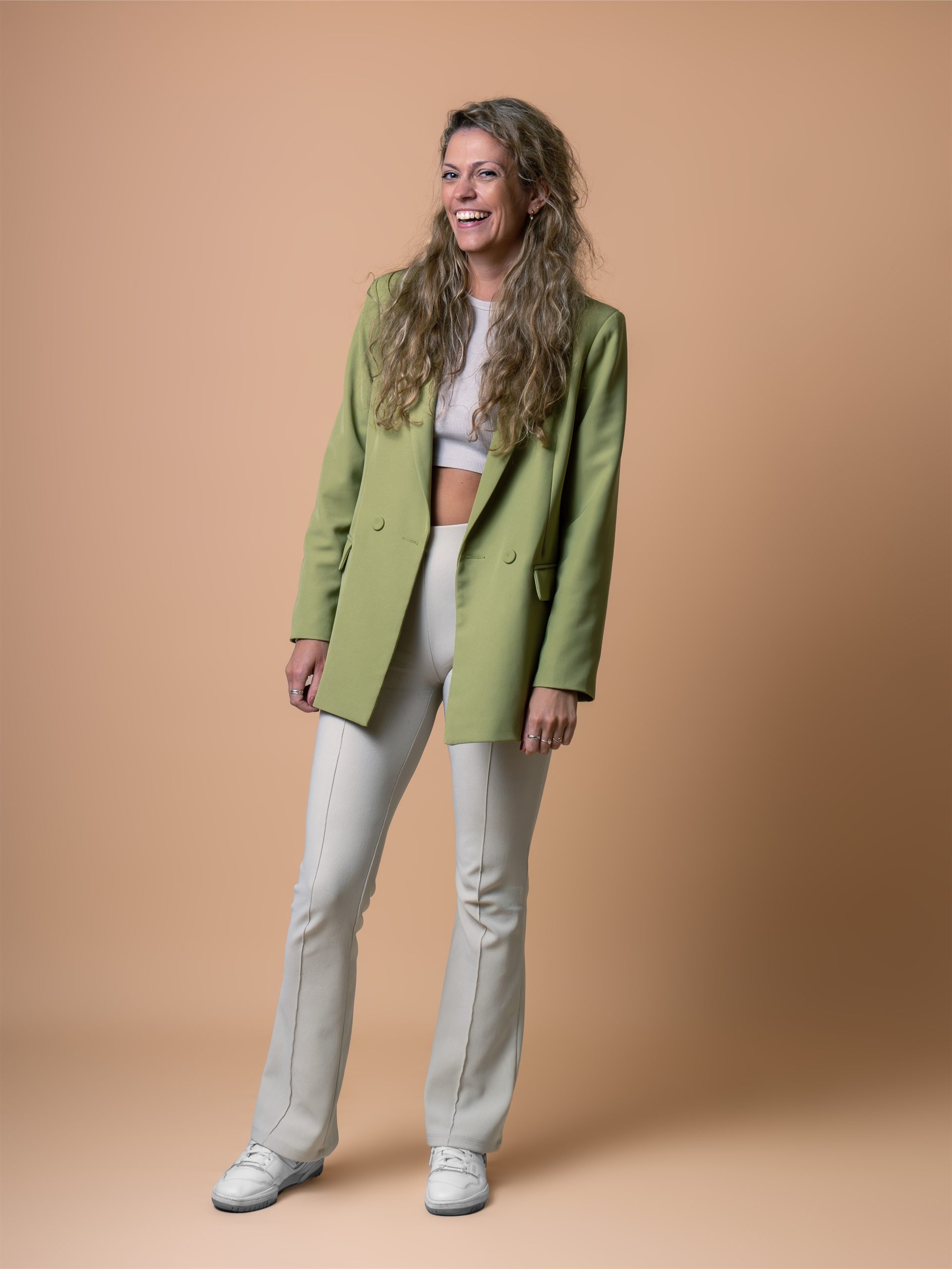 Staand zakelijk portret van een glimlachende vrouw in een groene blazer tegen een beige achtergrond.